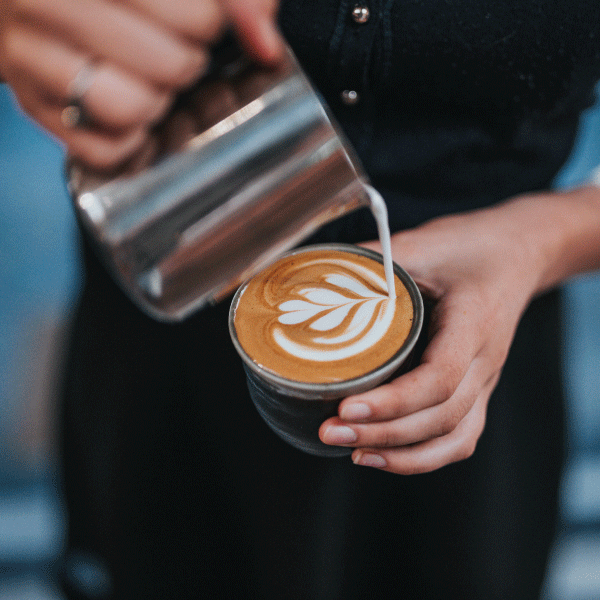 Barista haciendo latte arte con pitcher y taza negra